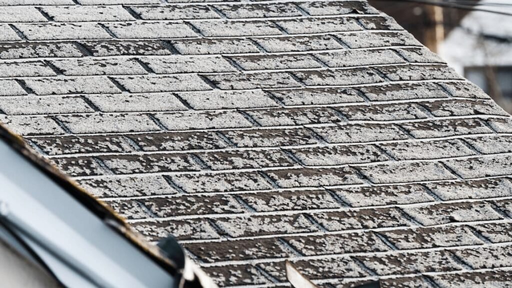 Close-up view of asphalt shingles showing granule loss, revealing bare spots and exposed asphalt on a roof.